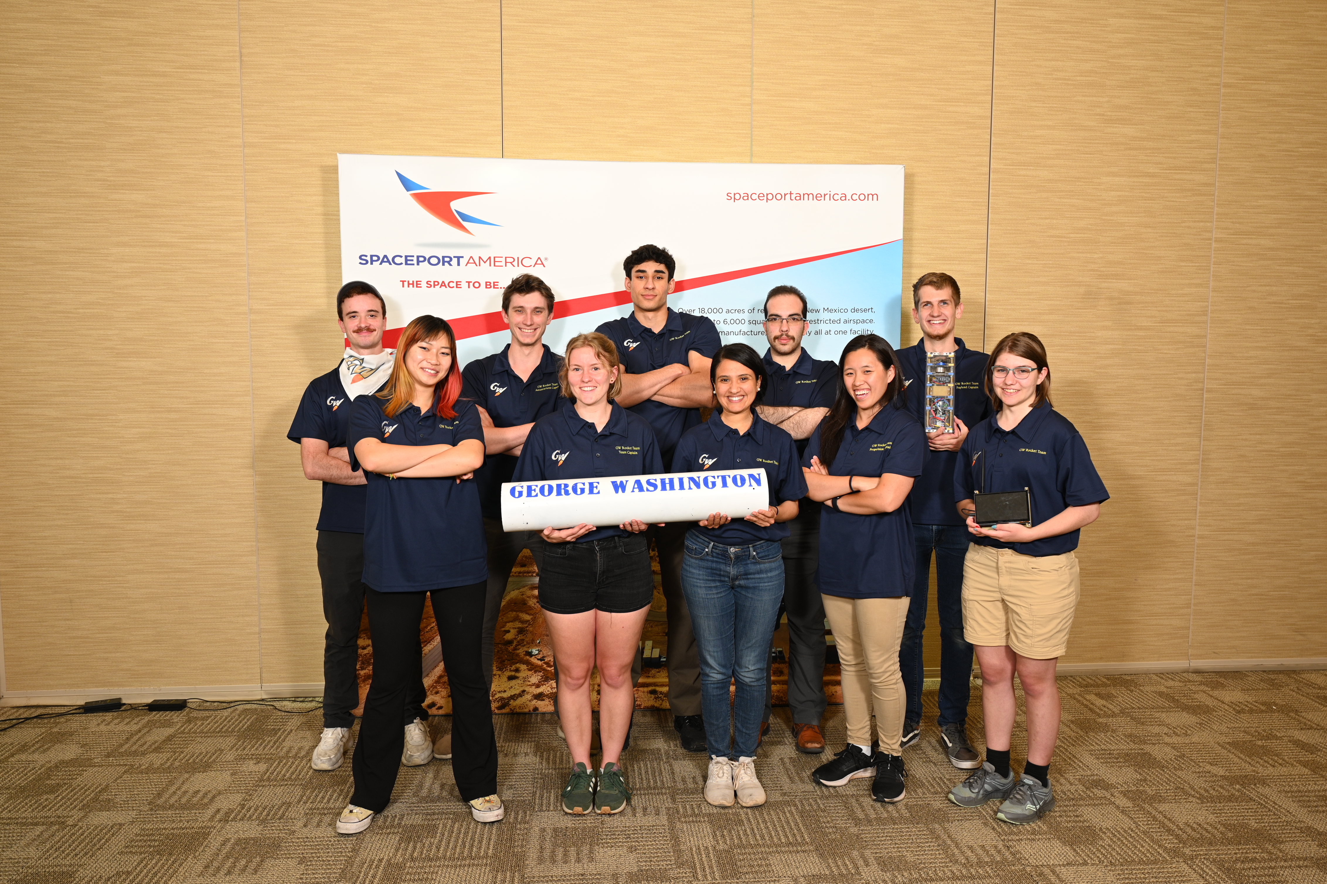 The 2023 GW Rocket Team smiling in front of a Spaceport America banner